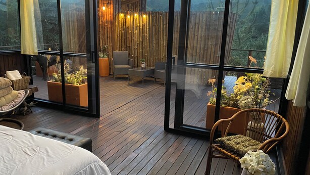 A spacious balcony with wooden flooring, wicker furniture, and potted plants.
