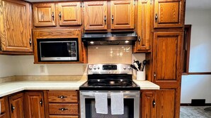 A kitchen with wooden cabinets, a microwave, an oven, and a countertop. - Spacious 3BR 2BA Gem Close to Downtown, 30 day min (Eau Claire)