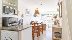 A compact kitchen with a washing machine, microwave, and toaster. There is a dining area with wooden chairs and a table.