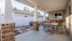En udendørs terrasse med en murstenspejs, et spisebord med stole og et overdækket siddeområde.