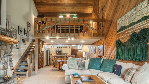 A spacious living area with a high ceiling, wooden beams, a staircase, and a kitchen in the background. - 3 Bedrooms + Loft townhome in Snowcreek Phase 3,  Private Pool Table Sleeps 6 Guests, Dog Friendly (Mammoth Lakes)