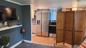 Un espace de vie compact comprenant un coin cuisine, un téléviseur fixé au mur et un tapis gris à longues mèches.