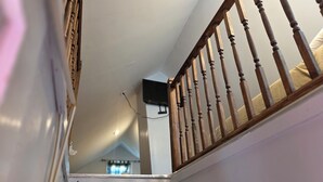 Un escalier avec des balustrades en bois et une main courante blanche, menant à une pièce dotée d’une fenêtre et d’un luminaire fixé au plafond.