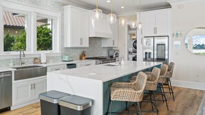 Una cocina moderna con armarios blancos, una isla grande con taburetes de bar, electrodomésticos de acero inoxidable e iluminación colgante.