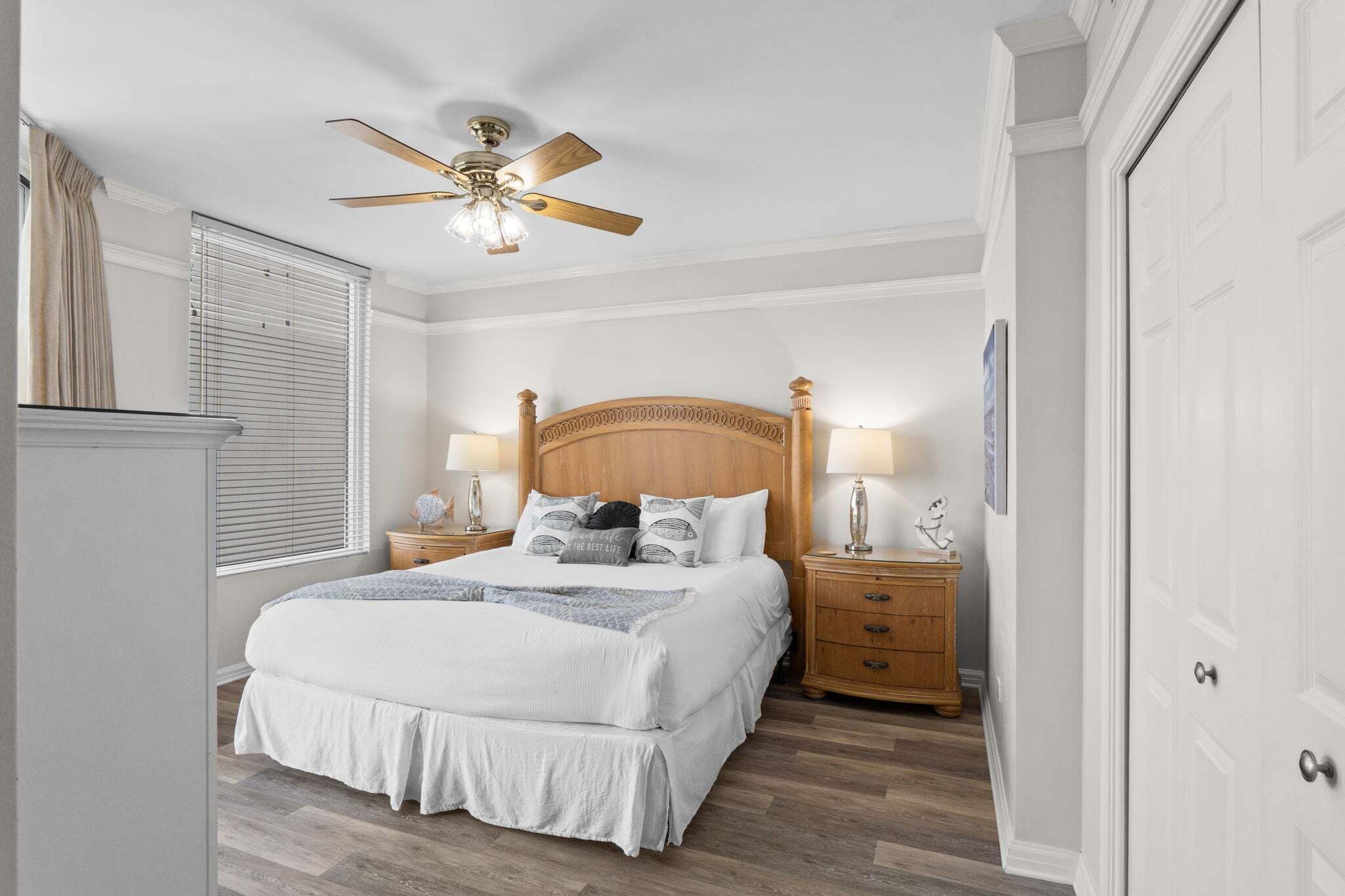 A bedroom with a bed, nightstands, a ceiling fan, and a door.