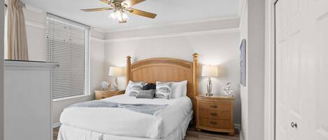 A bedroom with a bed, nightstands, a ceiling fan, and a door.