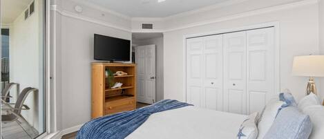 A bedroom with a bed, a television on a wooden stand, a ceiling fan, and a door.
