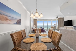A dining area with a large table, wicker chairs, a central vase, and a view of the ocean through large windows.