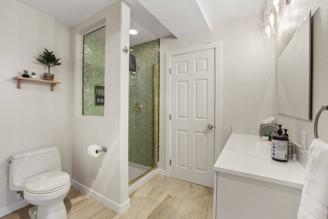 A bathroom with a toilet, a shower with a glass door, a sink with toiletries, and a mirror.