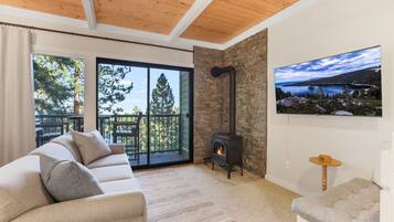 Una sala de estar acogedora con un sofá, una chimenea y un balcón con vistas a árboles y un lago.