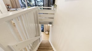 Eine Treppe mit weißen Geländern und Teppichstufen führt zu einem Raum mit einem Bett und einem Fenster.