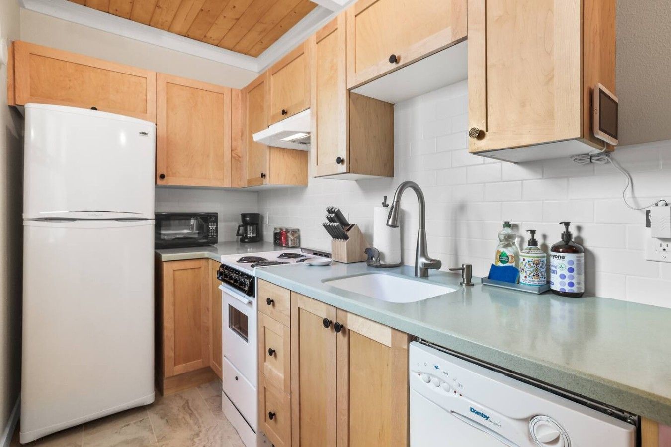 Una cocina con armarios de madera, un refrigerador blanco, una estufa, un lavamanos y un lavavajillas.