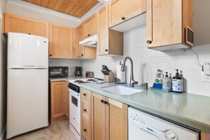 Une cuisine avec des meubles de rangement en bois, un réfrigérateur blanc, une cuisinière, un évier et un lave-vaisselle.