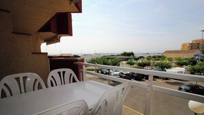A balcony with a table and chairs, overlooking a parking area and buildings. - ROCMAR Apartment opposite the port of Roses. (Roses)