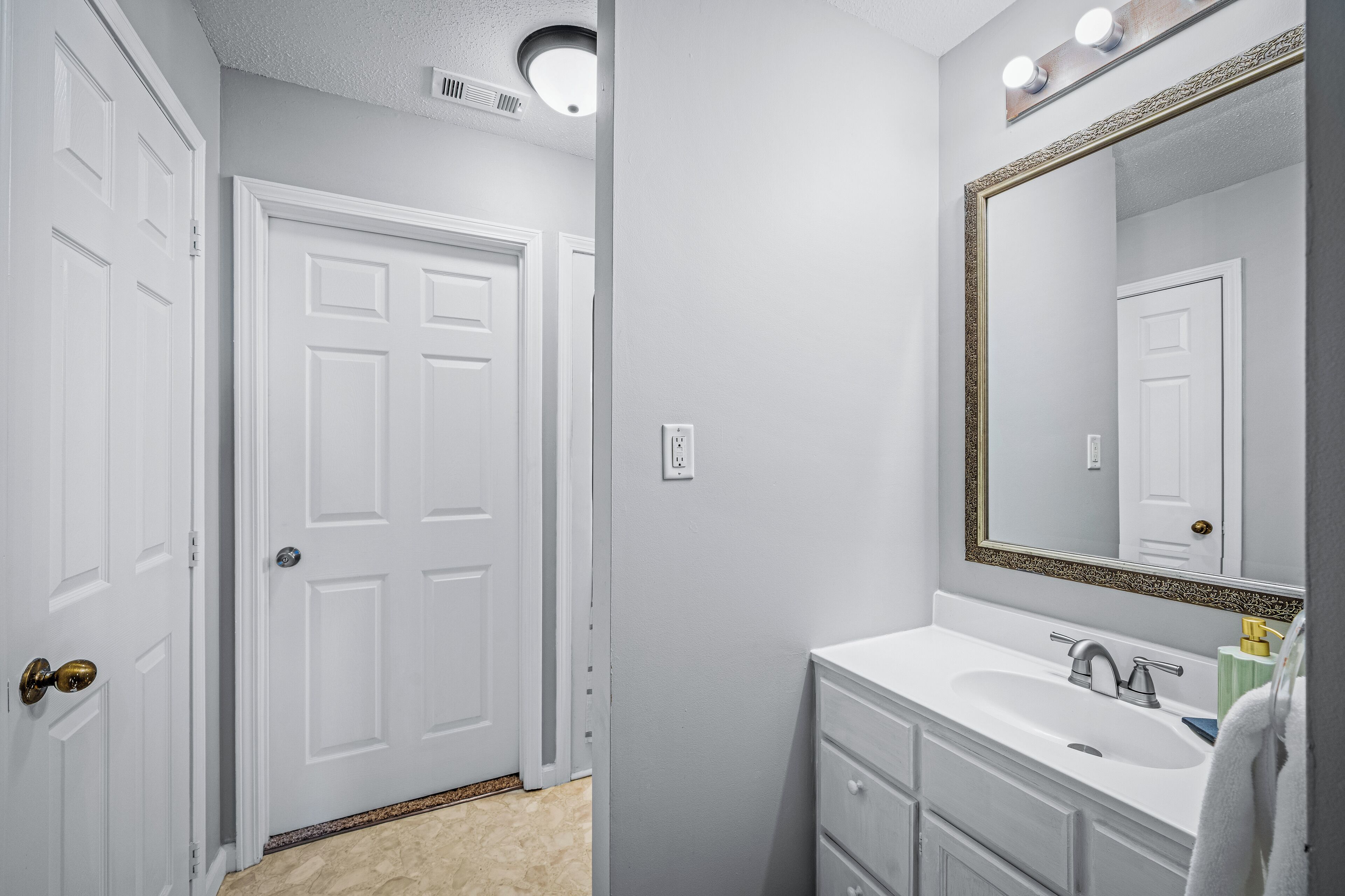A bathroom with a white vanity, a large mirror with a gold frame, and a white door.