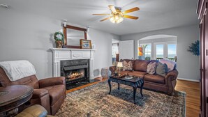 A living room with a fireplace, leather sofa, and a ceiling fan. - Best View Above Mentone - High Brow House - Elevate to Escape (Mentone)