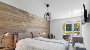 A modern bedroom with a large bed, wooden panel wall, and a view of the outdoors. - Central Parc 2 by Interhome (Crans-Montana)