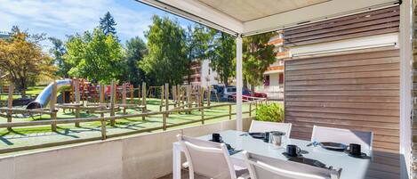 A covered outdoor area with a table and chairs, a playground in the background, and a view of a residential area.