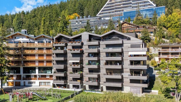 A modern multi-story hotel with balconies, a playground, and a lake view. - Central Parc 2 by Interhome (Crans-Montana)
