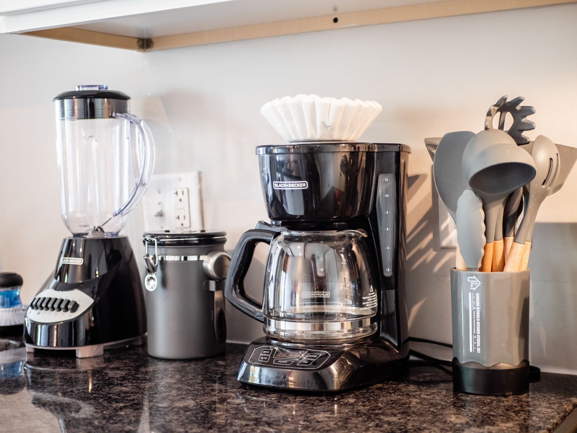 A kitchen counter with a blender, a coffee maker, a kettle, and a utensil holder.