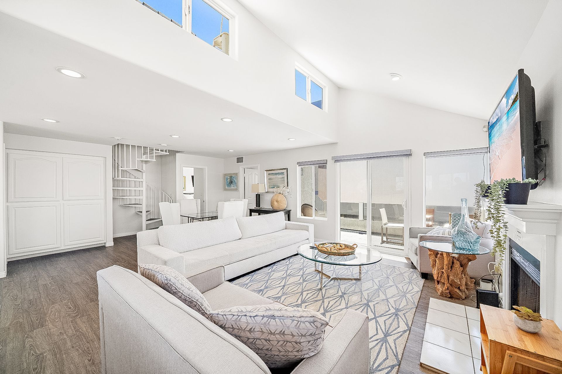 A spacious living room with a high ceiling, a built-in fireplace, and a large window offering a view of the outdoors.