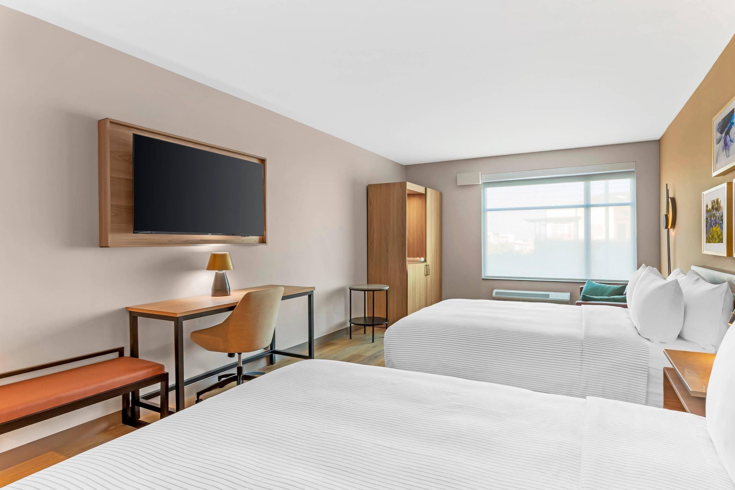 Habitación de hotel con dos camas, un escritorio con silla, televisión, armario y ventana.