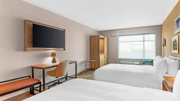 Habitación de hotel con dos camas, un escritorio con silla, televisión, armario y ventana.