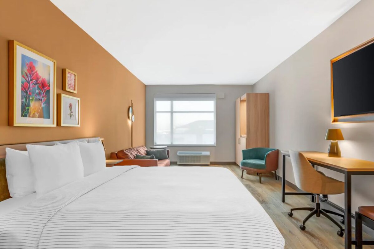 Habitación de hotel con una cama grande, un escritorio, una silla, un ventanal y cuadros en la pared.