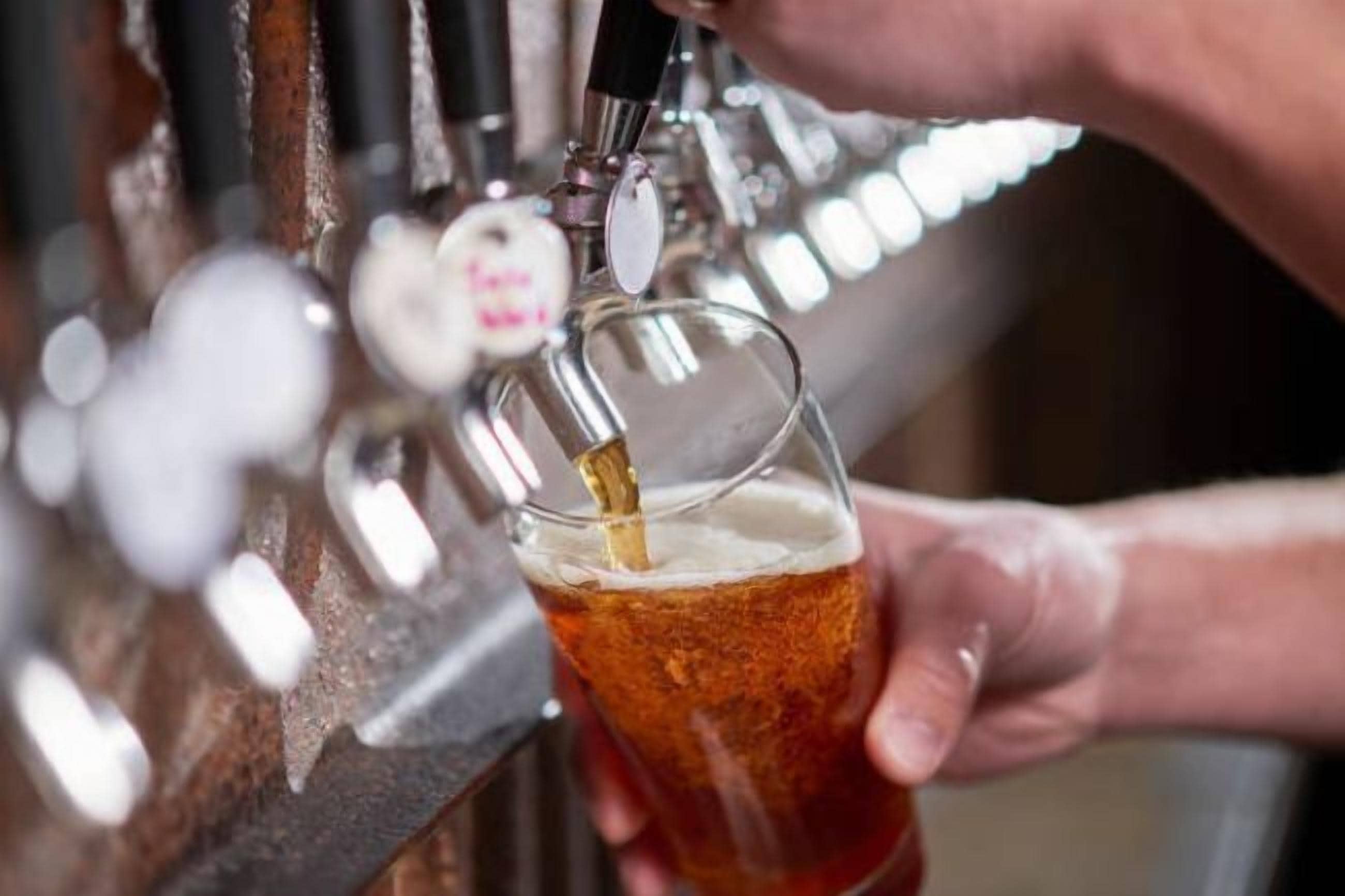 A hand holding a glass receiving a beverage from a tap.