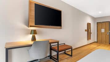 Ein Hotelzimmer mit einem Bett, einem Schreibtisch mit Stuhl, einem an der Wand befestigten Fernseher und einer Tür.
