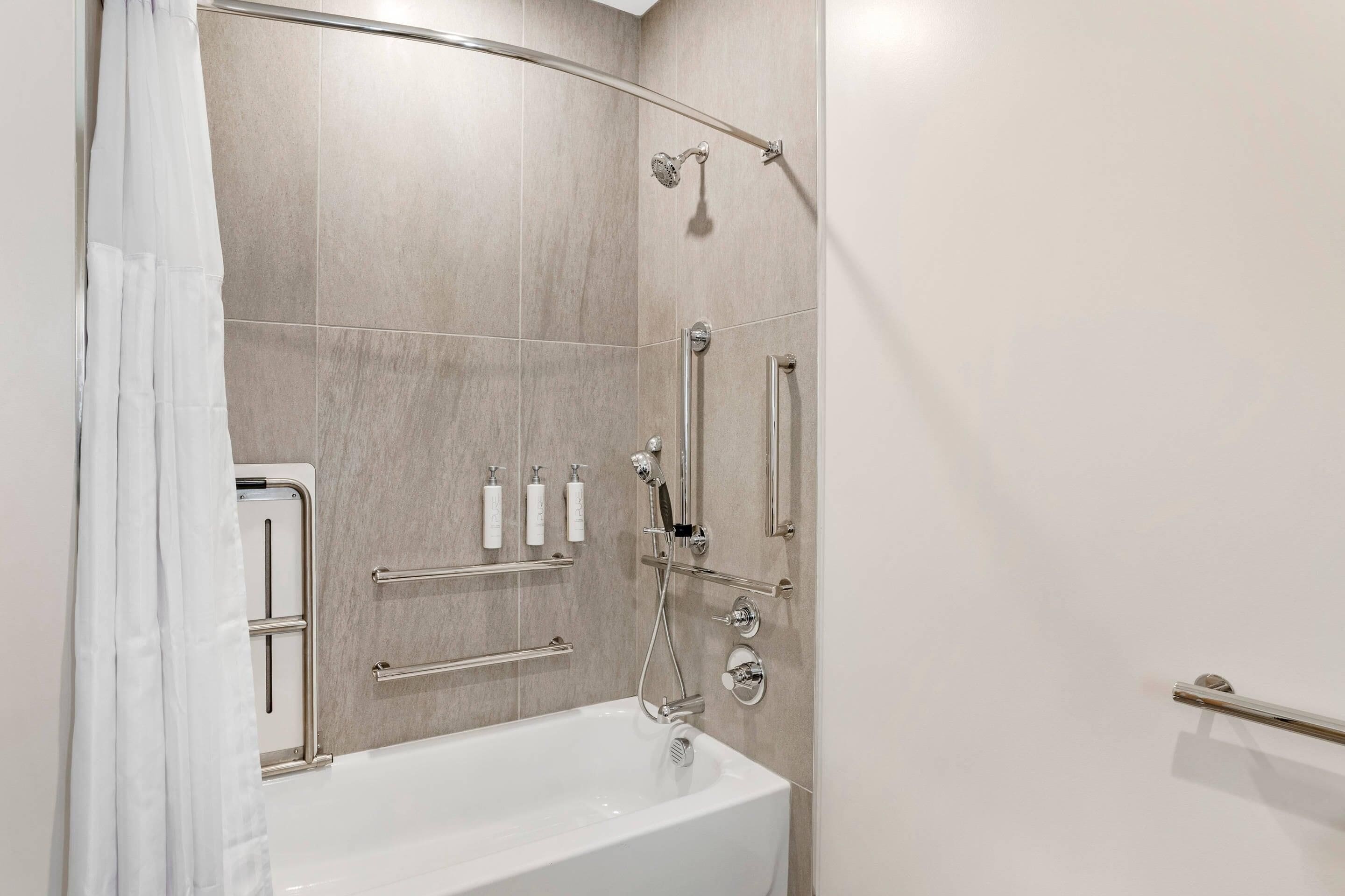 Een moderne badkamer met een badkuip, douche en handgrepen.