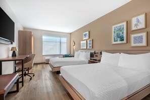 Habitación de hotel con dos camas, un escritorio, una silla, un televisor y obras de arte en las paredes.