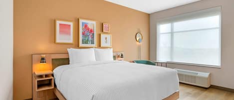 A hotel room with a bed, bedside tables, wall art, a desk, and a large window.