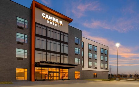 A modern hotel building with a prominent sign, large windows, and a covered entrance.