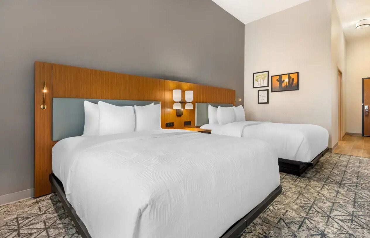 A hotel room with two beds, a wooden headboard, a patterned rug, and wall-mounted artwork.