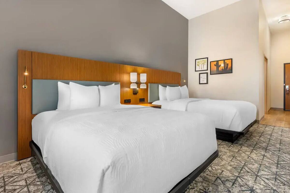 A hotel room with two beds, a wooden headboard, a patterned rug, and wall-mounted artwork.