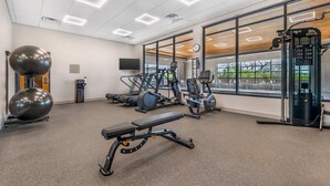 Une salle de sport équipée de matériel d’exercice, d’un banc et de grandes fenêtres.