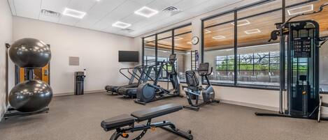 A gym with exercise equipment, a bench, and large windows.