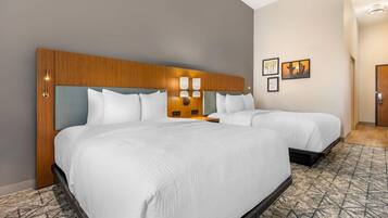 A hotel room with two beds, a wooden headboard, wall-mounted lights, and framed pictures.