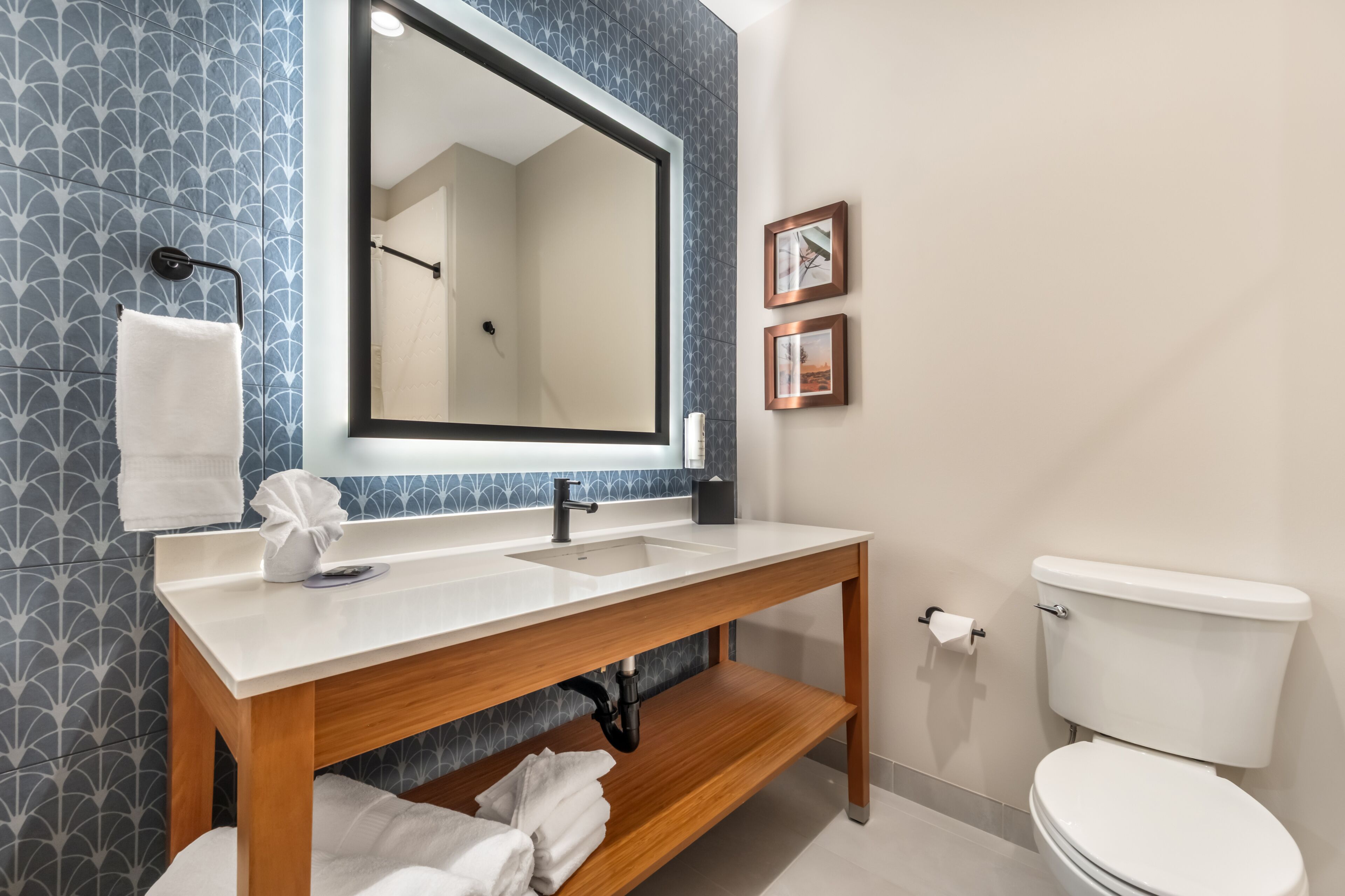 A bathroom with a wooden vanity, a large mirror, a toilet, and patterned wall tiles.