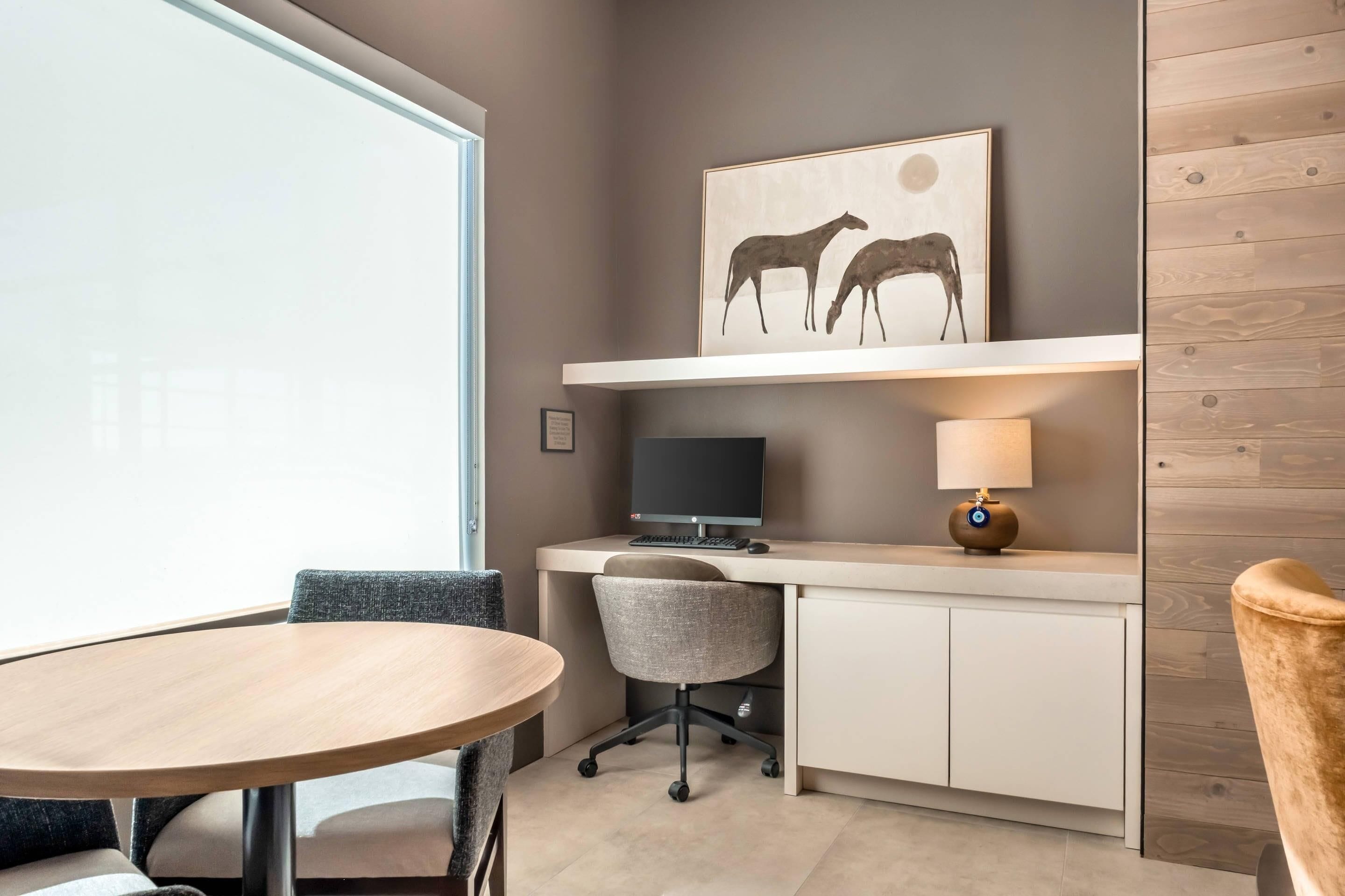 A modern office space with a desk, computer, chair, and round table.