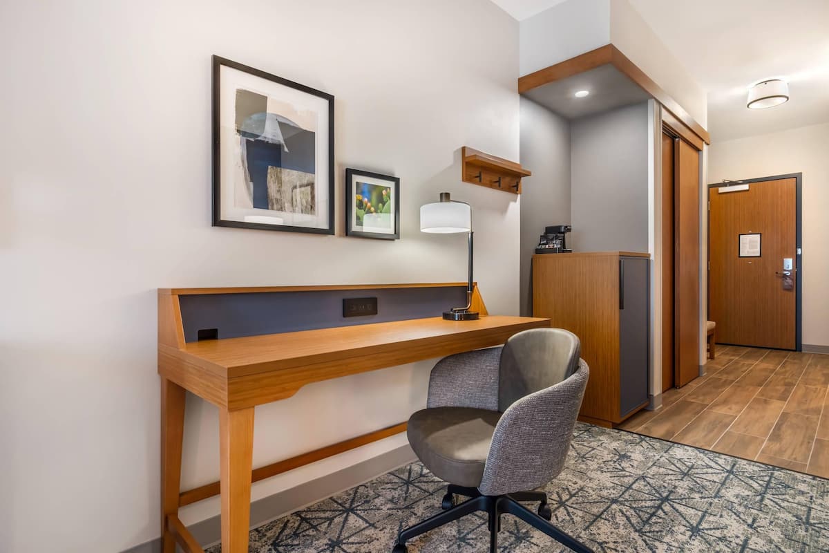A hotel room with a wooden desk, a chair, a lamp, and two framed pictures on the wall.