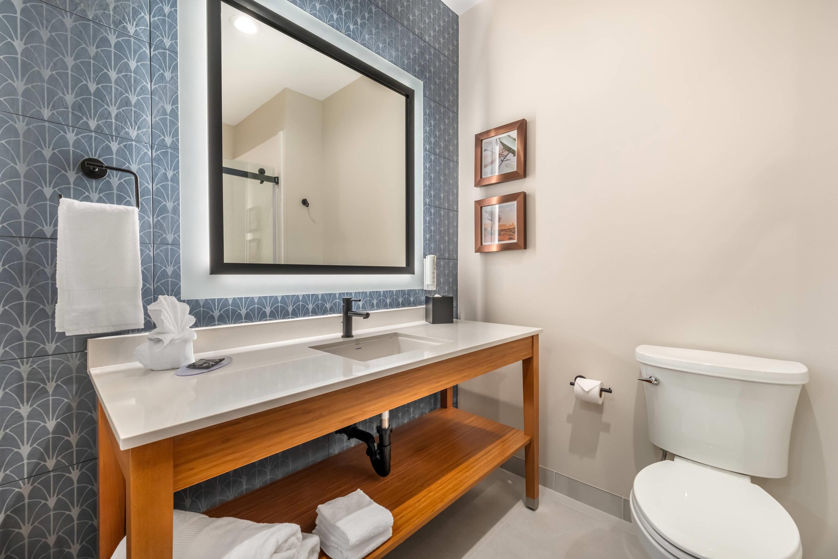 A bathroom with a wooden vanity, a large mirror, a white toilet, and patterned wall tiles.