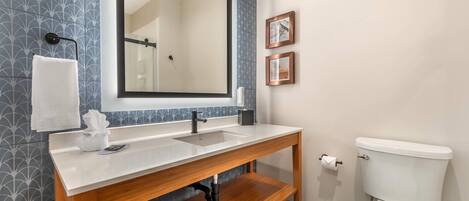 A bathroom with a wooden vanity, a large mirror, a white toilet, and patterned wall tiles.