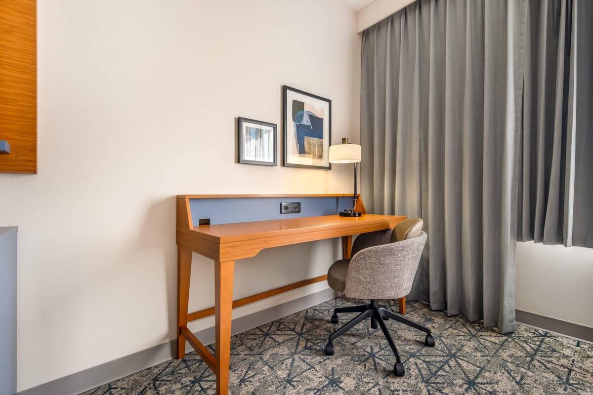 A hotel room with a wooden desk, a chair, a lamp, and two framed pictures on the wall.