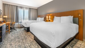 Une chambre d’hôtel avec deux lits, un bureau, une chaise et une grande fenêtre avec des rideaux.