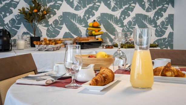 Un desayuno con un croissant, un vaso de jugo de naranja y un bol de fruta sobre una mesa.