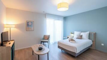 A modern hotel room with a bed, bedside table, lamp, chair, and a desk with a computer.