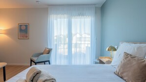 A hotel room with a bed, a chair, a nightstand, a lamp, and a painting on the wall. - Quality Aparthotel Limoges (Limoges)