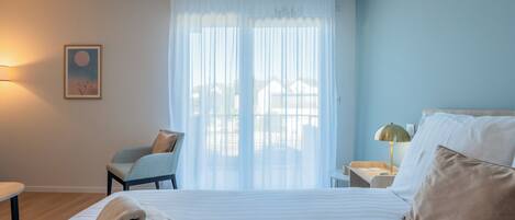 Una habitación de hotel con una cama, una silla, una mesita de noche, una lámpara y un cuadro en la pared.